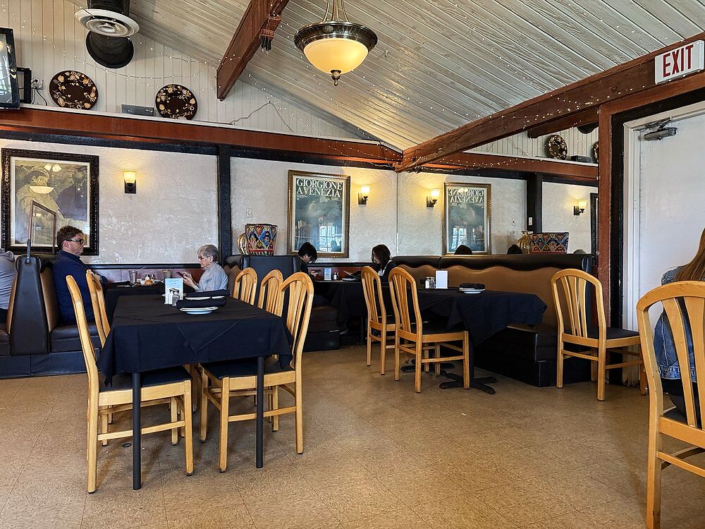 The dining room at Pasta Connection, wood-beam ceiling, black tablecloths, and warm string lights