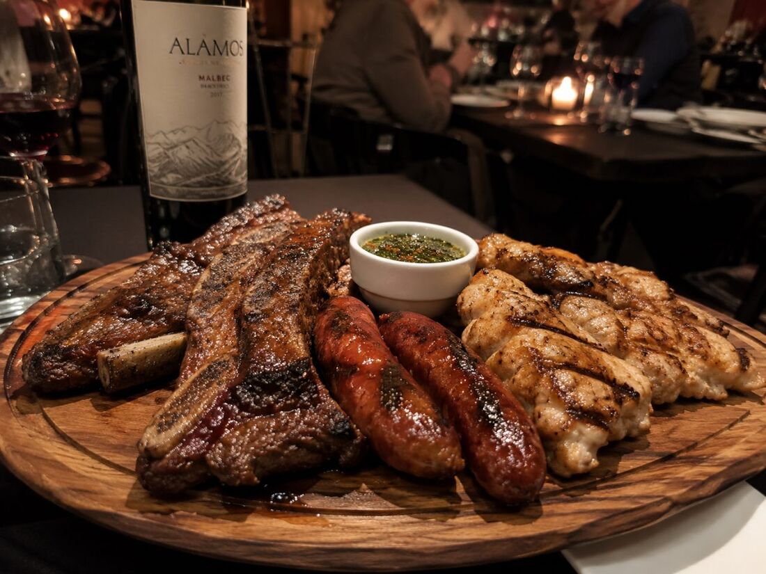 Argentine parrillada mixed grill with short ribs, chorizo, and chimichurri on a wood board