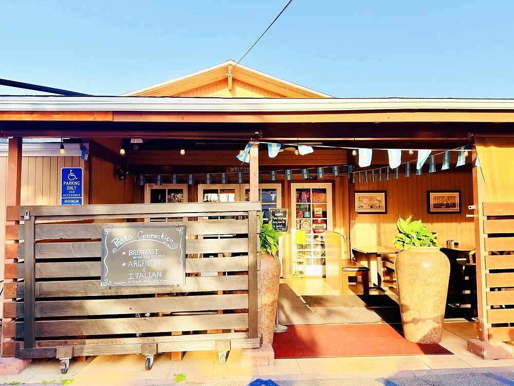 The covered patio entrance at Pasta Connection at golden hour, with the Argentine and Italian chalkboard sign