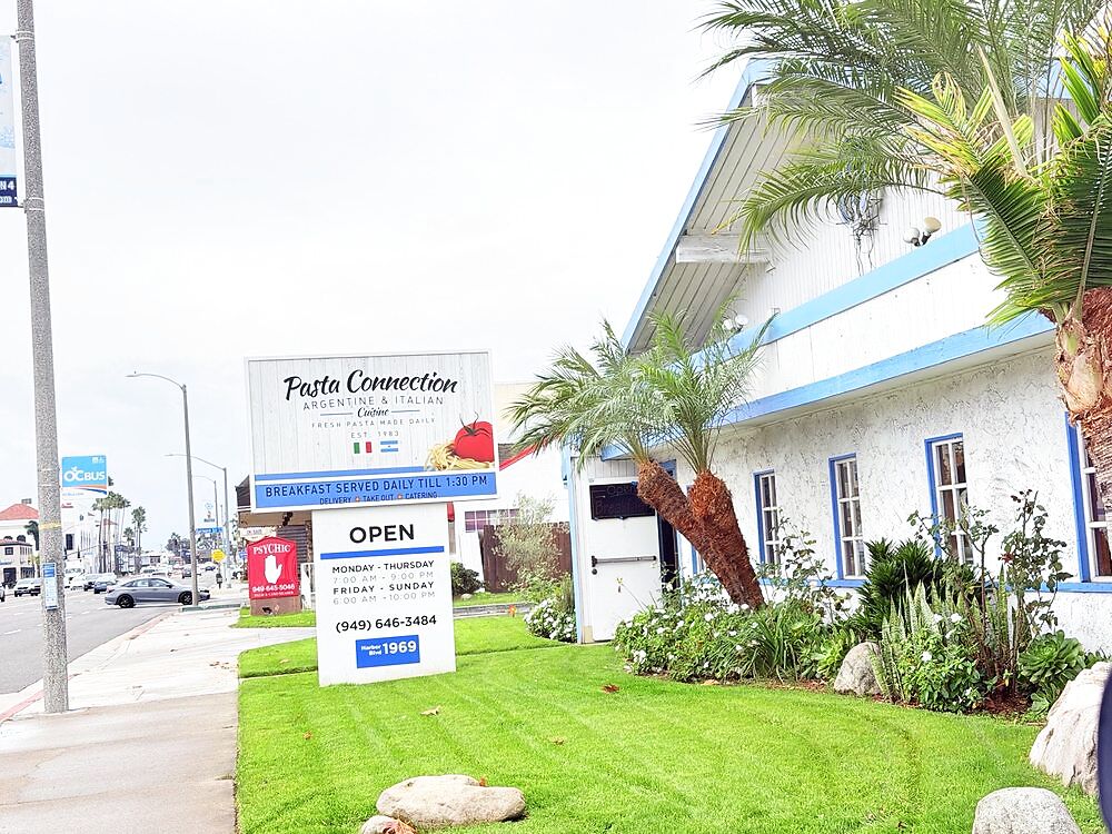 The Pasta Connection storefront on Harbor Blvd, a white building with blue trim, a palm tree, and the Argentine and Italian sign